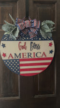 Load and play video in Gallery viewer, God Bless America Door Hanger | 19&quot; Patriotic Round Sign | Hand Painted Birch Wood | 4th of July Front Door Decor
